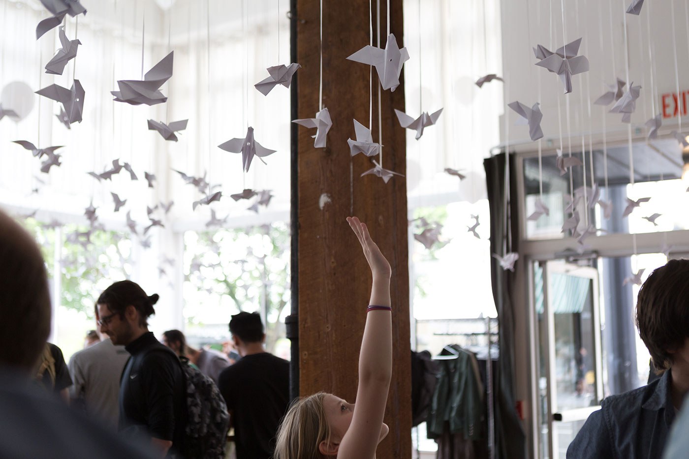 Woman reaching up to touch one of many paper cranes that are handing from the ceiling